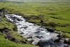 Vgar island, Faroes: hiker crossing a stream on the moorlands - photo by A.Ferrari